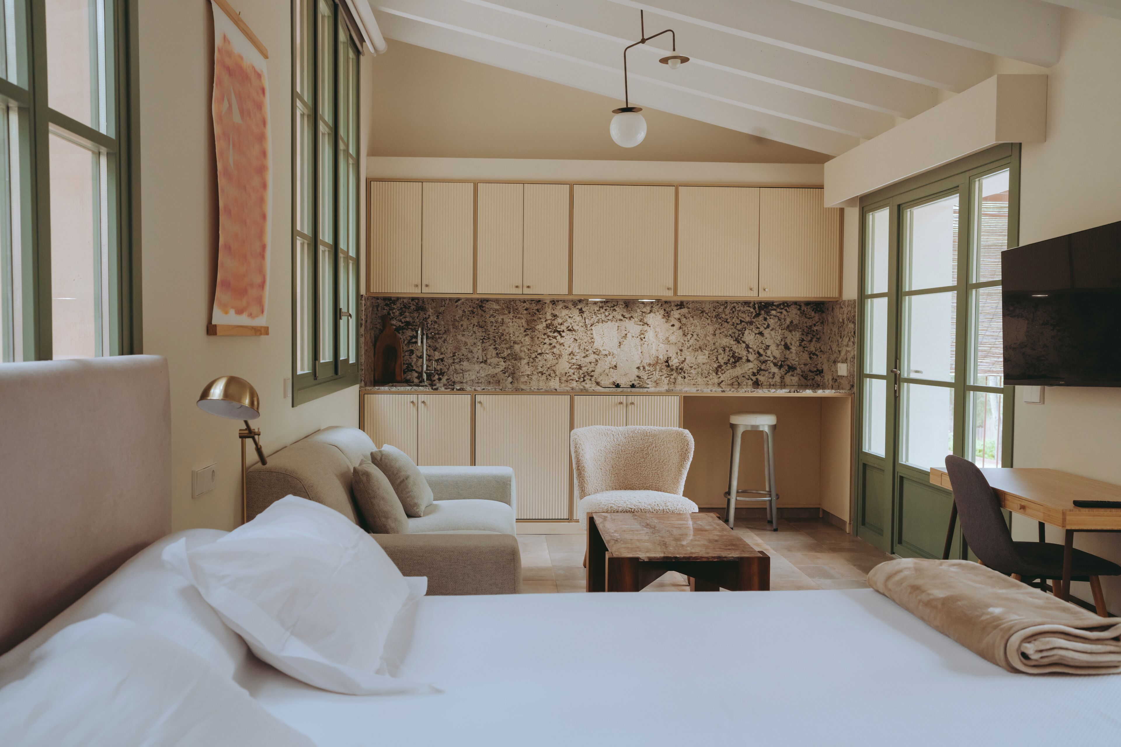 Habitación de hotel con cama, escritorio, silla, sofá y una zona de cocina con armarios y encimera.