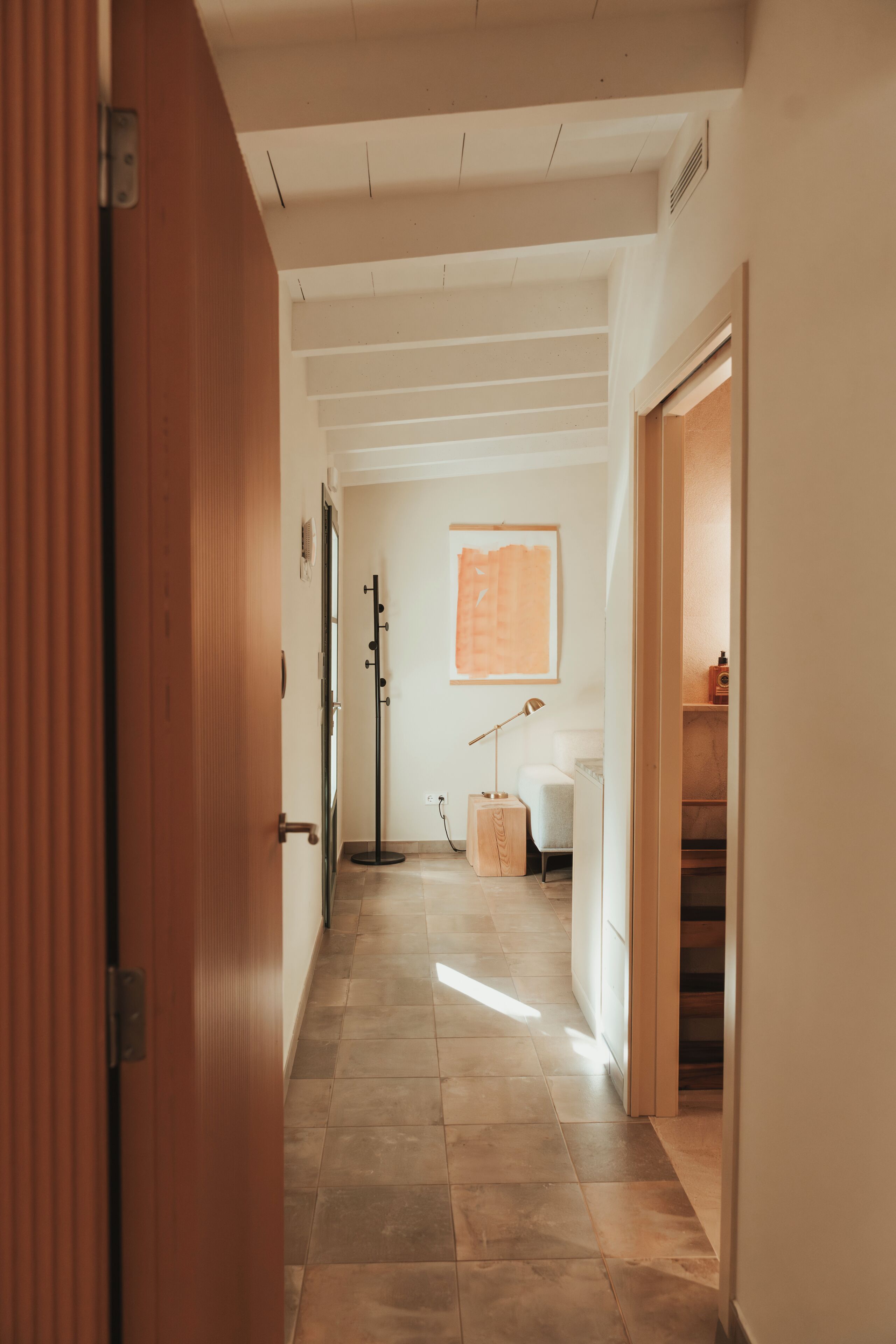 A hallway with a wooden door, a coat rack, a floor lamp, and a framed artwork on the wall.