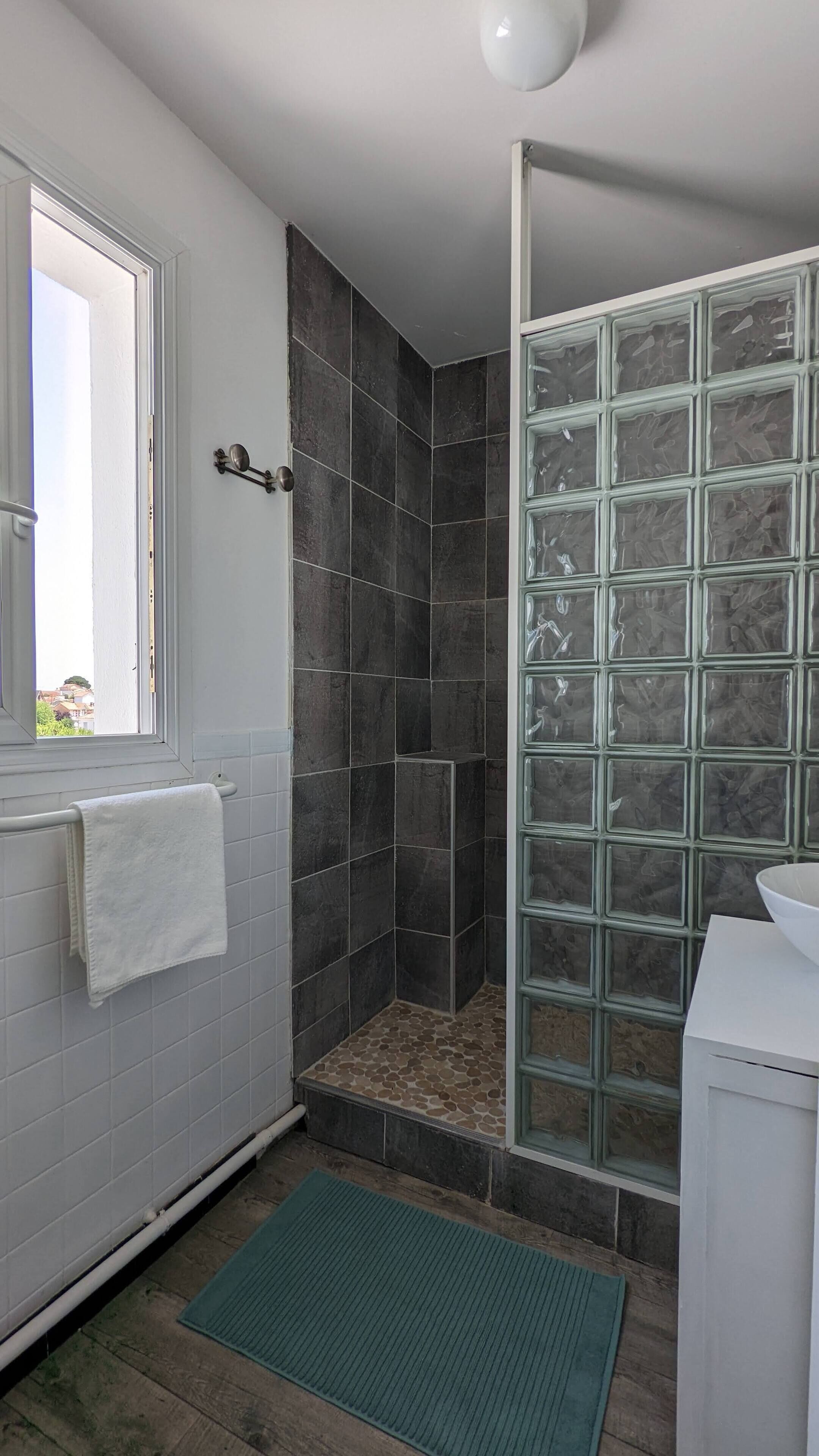 Een badkamer met een douche, een raam en een wastafel.