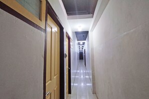 A corridor with a tiled floor, wooden doors, and a ceiling with recessed lighting. - Hotel O Benteng Kost (Jambi)