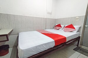 A single bed with a white and red bedspread, two pillows with red and white patterns, a wooden headboard, and a small bedside table.
