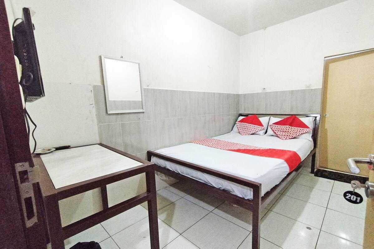 A small, clean room with a single bed, a bedside table, a mirror, and a door with a lock.