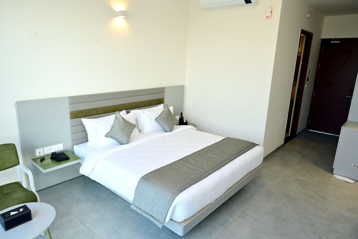 Une chambre d’hôtel comprenant un lit, une table de chevet, une chaise et une petite table avec un coffre.