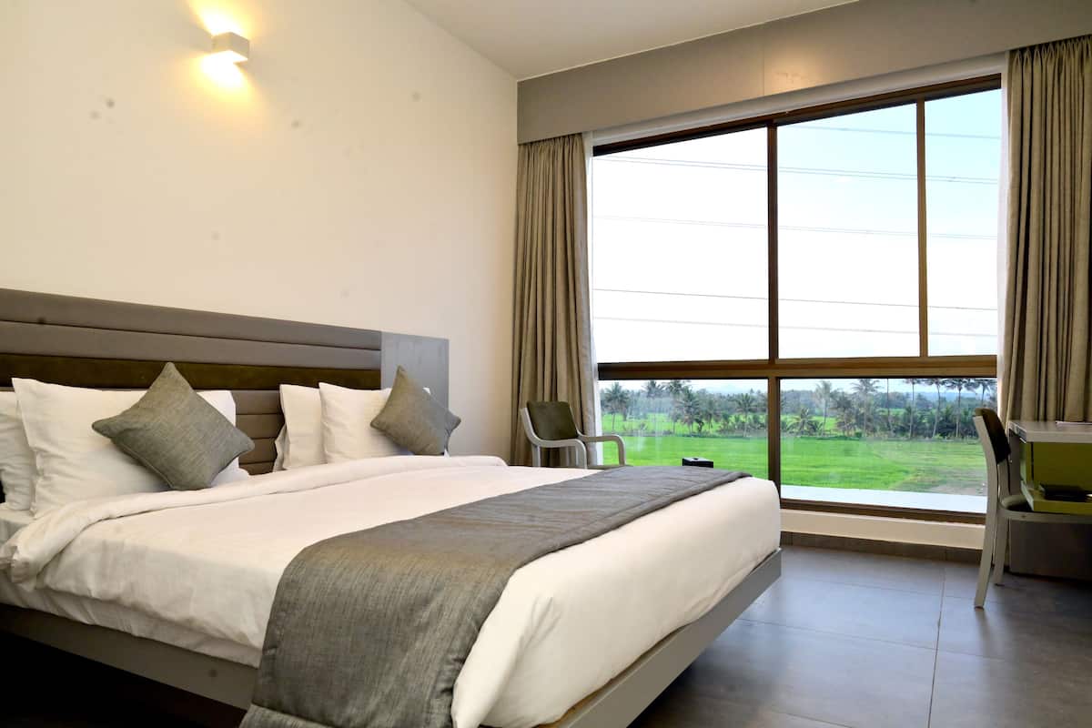 Une chambre d’hôtel avec un grand lit, un bureau et une vue sur un paysage verdoyant par la fenêtre.