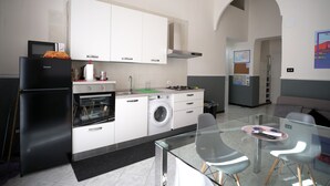 Une cuisine moderne avec des meubles blancs, un réfrigérateur noir, un lave-linge et une table à manger en verre, accompagnée de chaises.