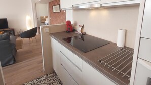 A compact kitchen with white cabinets, a black countertop, and a red appliance. There's a chair and a small table in the adjacent living area. - Family apartment with pool, gardens and parking in Malaga (Málaga)
