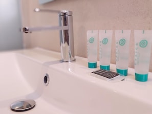 Kylpyhuoneen allas, jossa on krominen hana ja neljä pulloa hygieniatuotteita.