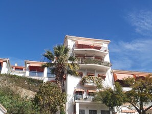 A multi-story building with balconies, a palm tree, and a clear blue sky. - Family apartment with pool, gardens and parking in Malaga (Málaga)