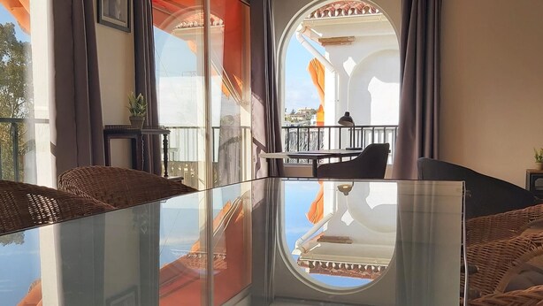 A modern room with a glass table, wicker furniture, and a balcony with a view. - Family apartment with pool, gardens and parking in Malaga (Málaga)