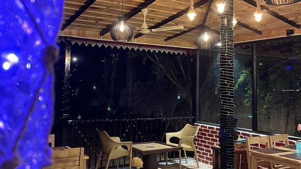 An outdoor dining area with wooden tables and chairs, a brick wall, and hanging pendant lights. - Sangita Resorts Naukuchiatal (Nainital)