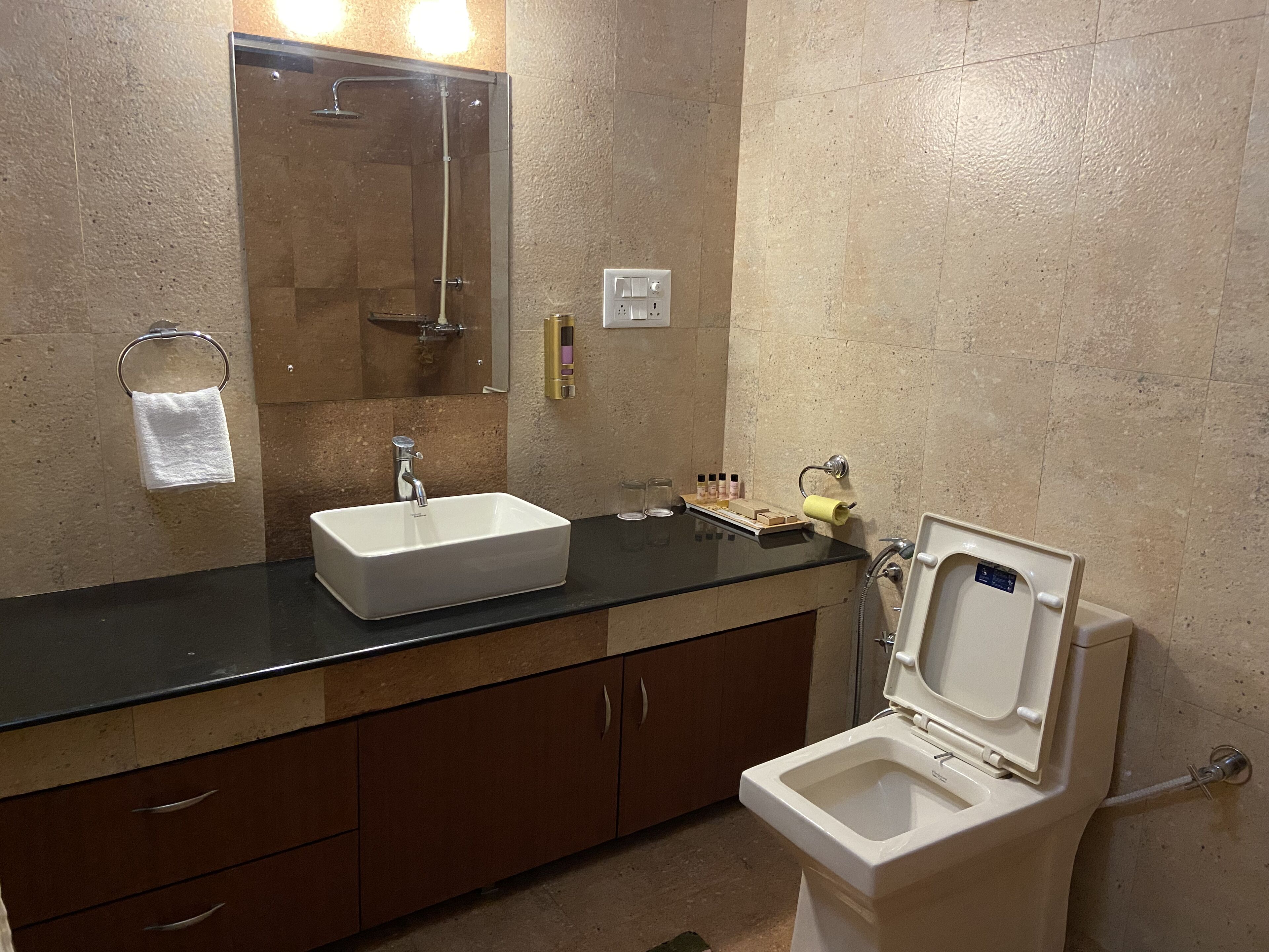 Een badkamer met een wastafel, spiegel, handdoekhouder, toilet en een klein plankje met toiletartikelen.