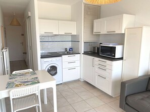 A compact kitchen with a washing machine, microwave, and a dining area with a table and chairs. - T1 with balcony, air con, wifi, pets OK in Balaruc-les-Bains (Balaruc-les-Bains)