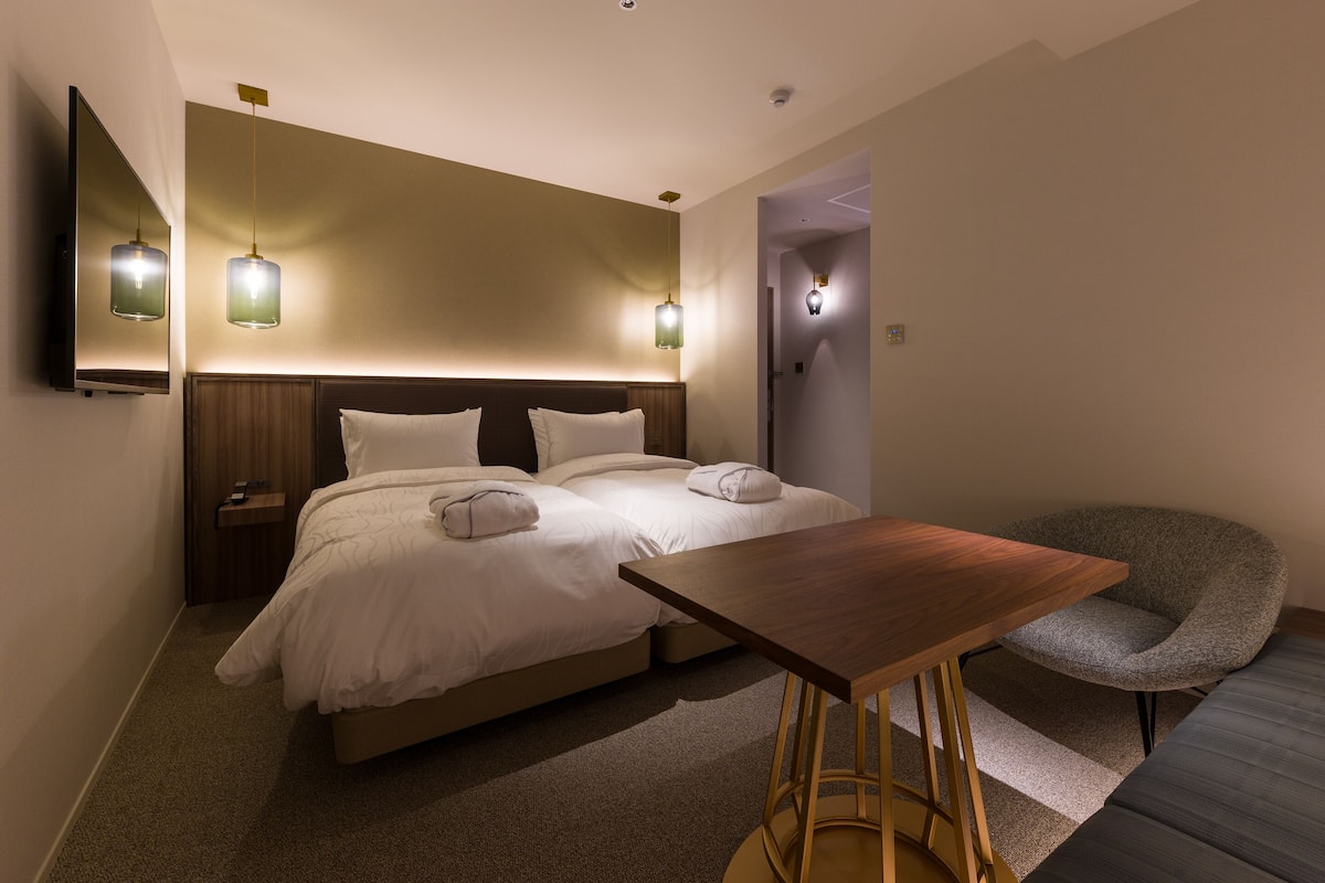 A hotel room with a bed, bedside tables, a chair, and a small table.