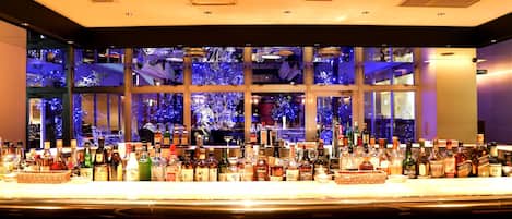 A bar with a variety of liquor bottles and a view of a cityscape through large windows.