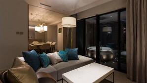 Et moderne hotelværelse med sofa, spiseplads og et stort vindue med gardiner.