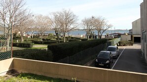 A parking area with cars, a building, and a body of water in the background. - Bright Studio with Terrace, Near Shops and Thermal Baths (Balaruc-les-Bains)
