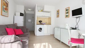 A compact living space with a sofa, a washing machine, a small kitchenette, and a TV. - Modern Studio with Terrace, AC, and Parking (Balaruc-les-Bains)