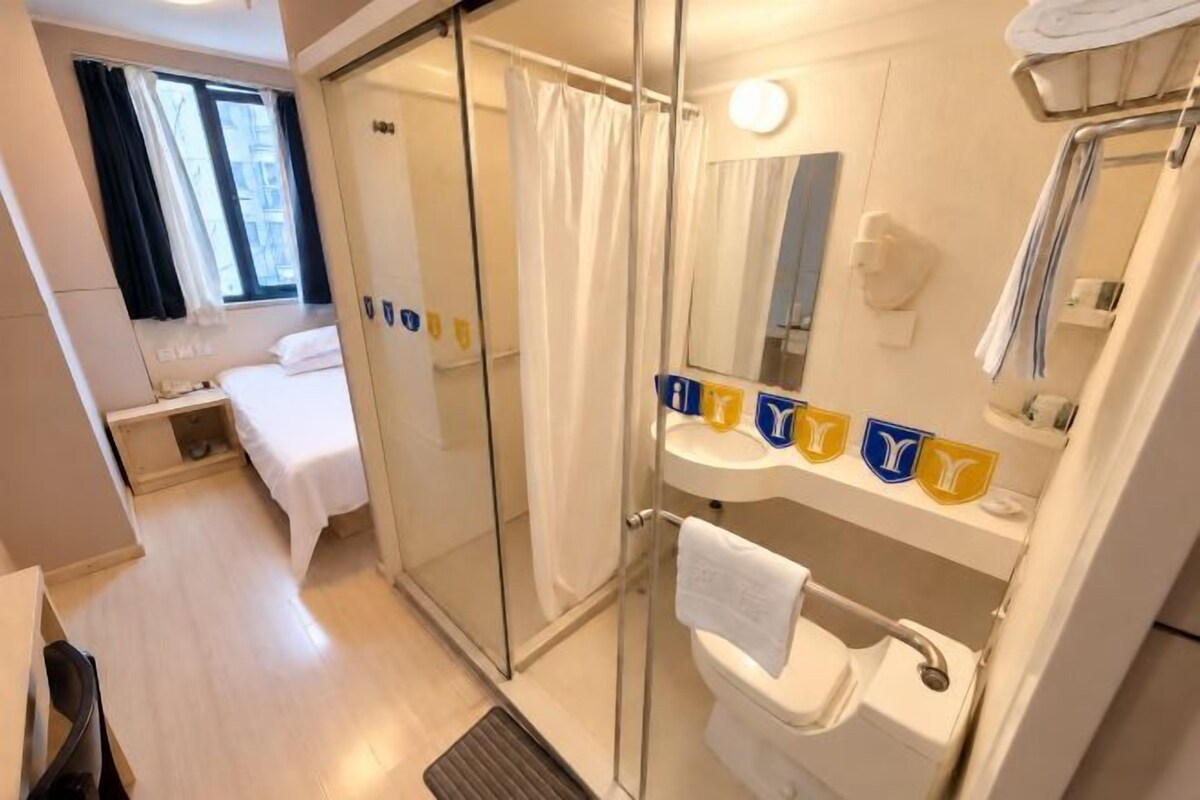 A hotel room with a bed, a shower, a toilet, and a sink.