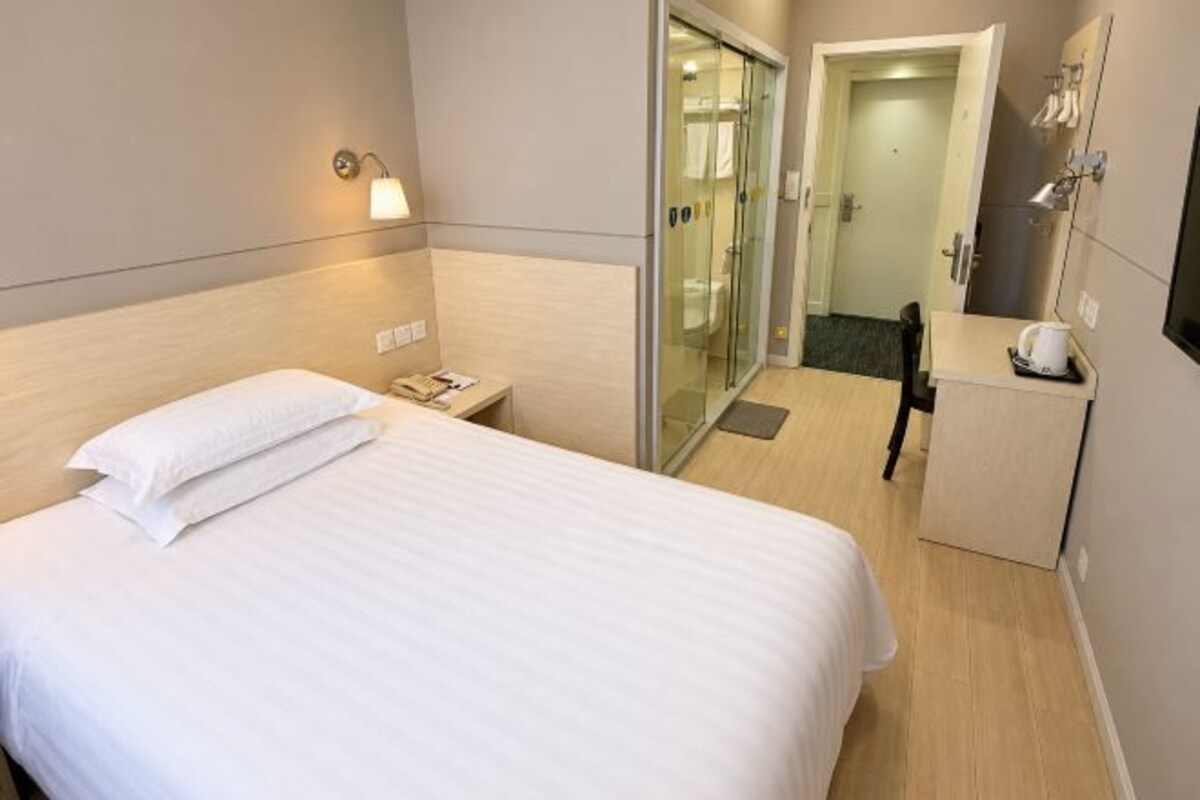 A hotel room with a bed, bedside table, lamp, and a door leading to a bathroom.