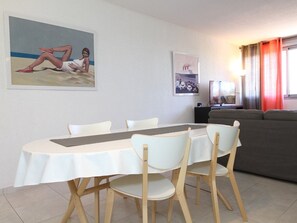 A dining area with a round table and four chairs, a grey sofa, and two framed pictures on the wall.
