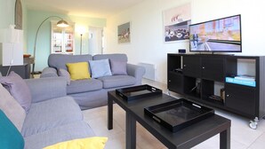 Una sala de estar moderna con un sofá gris, una mesa de centro negra y un televisor sobre un mueble negro.