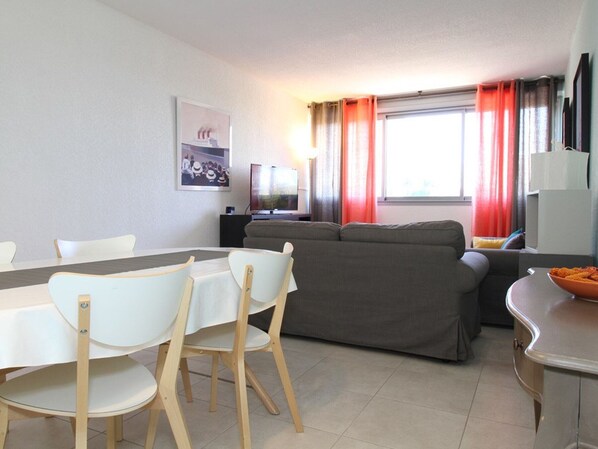 A modern living room with a dining area, a gray sofa, and a TV.