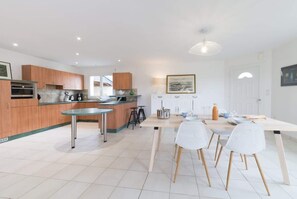 A modern kitchen with wooden cabinets, a dining table with chairs, and a kitchen island. - Ty Bihan - Pretty one-storey house near the sea (Ploudalmézeau)