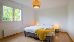 Et soveværelse med seng, sengeborde, en radiator og et vindue med udsigt til grøn vegetation.