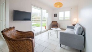 En stue med et fladskærms-tv, fletmøbler, en grå sofa og et rundt, lille bord.