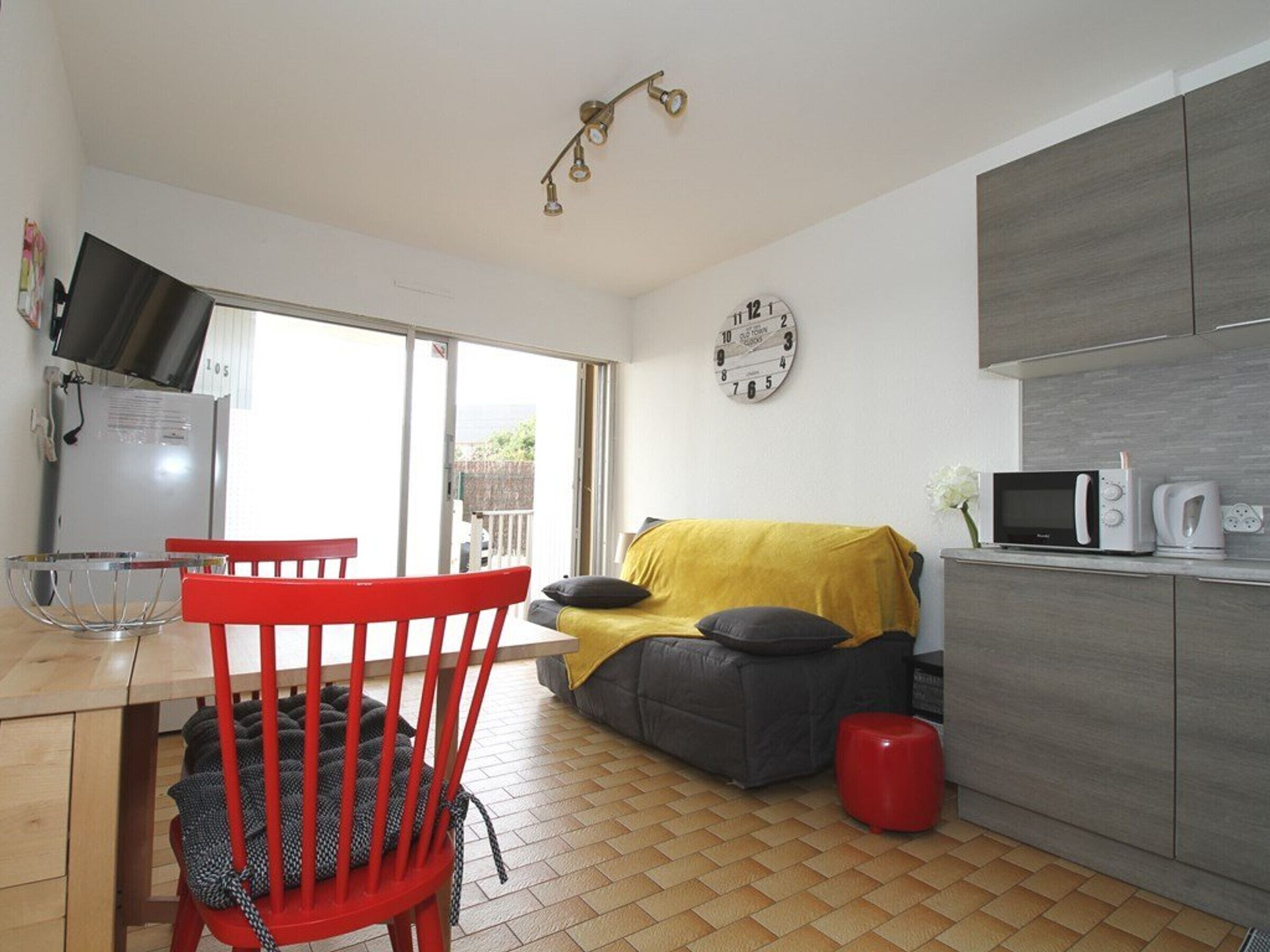 A compact living space with a dining area, a sofa, a kitchen with modern appliances, and a large window.