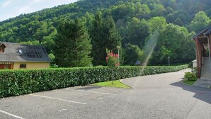 Un estacionamiento con un edificio a la izquierda, un árbol con flores rosadas en el centro y una montaña al fondo.