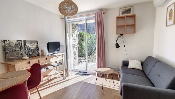 Un salón moderno con un sofá gris, un escritorio de madera con una computadora, una silla roja y una mesa de comedor con una silla roja.