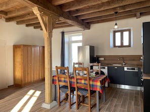 Una cocina rústica con vigas de madera, una mesa de comedor con sillas, un refrigerador y una ventana con cortinas.