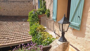 Un patio con techo de tejas, macetas de lavanda, un farol negro y un muro de piedra.