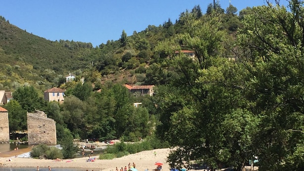 Una playa con agua cristalina, gente nadando y tomando el sol, y edificios al fondo.