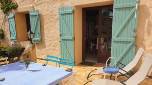 Un patio al aire libre con una mesa, sillas, una puerta y un muro con contraventanas.