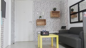 A room with a white brick wall, a grey sofa, a yellow table, and wooden shelves.