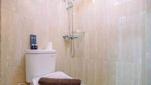A bathroom with a toilet, a shower, and a towel on the seat. - Comfort And Cozy Living Studio Room At Tifolia Apartment (Jakarta)