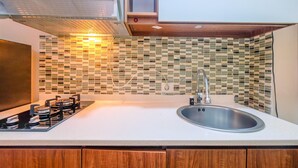A kitchen with a gas stove, a sink, and a tiled backsplash. - Comfort And Cozy Living Studio Room At Tifolia Apartment (Jakarta)