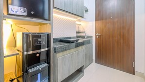A compact kitchen with a GEA water dispenser, a built-in oven, and a wooden door. - Great Choice And Comfortable Studio Transpark Cibubur Apartment (Depok)