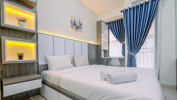 A modern bedroom with a bed, bedside tables, a wall-mounted shelf with plants, a painting, and a window with curtains. - Great Choice And Comfortable Studio Transpark Cibubur Apartment (Depok)
