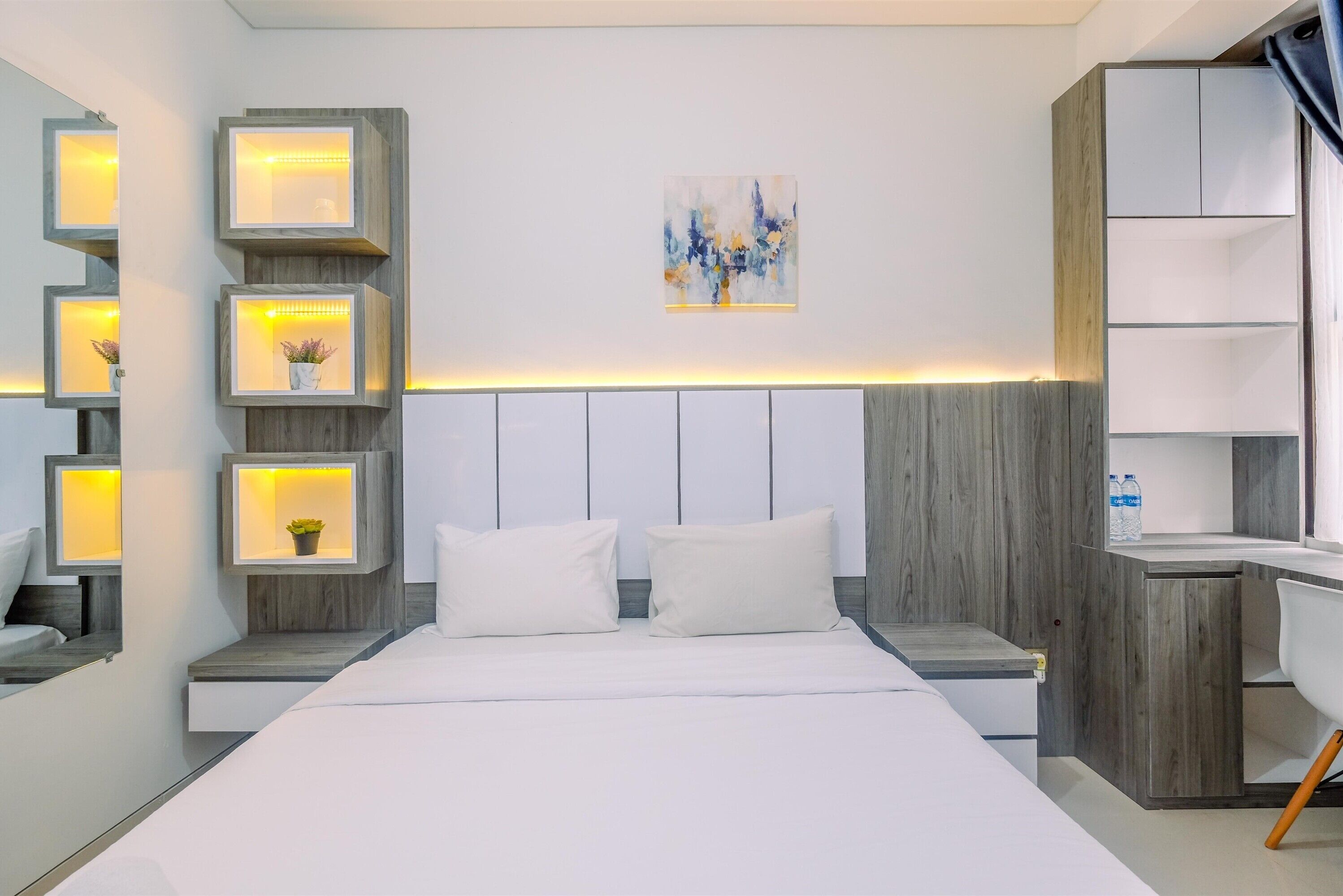 Une chambre d’hôtel moderne avec un grand lit, des tables de chevet dotées d’étagères éclairées, un bureau et une armoire.