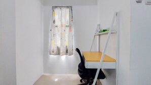 A small office space with a white desk, black office chair, and a white shelf with a few items.