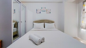 A neatly made bed with rolled white towels, a wooden headboard, and a white wall with three motivational posters.