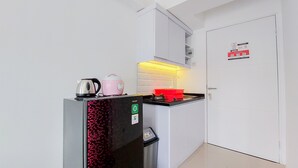 A compact kitchen with a refrigerator, a pink kettle, a red pot, and a sink.