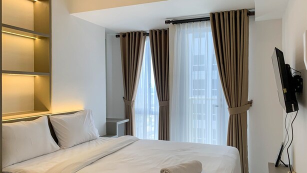 Una habitación de hotel con cama, televisión y ventana con cortinas.