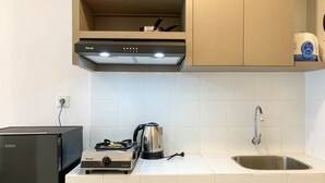 Una cocina con un refrigerador negro, una estufa a gas, un hervidor y un lavamanos.