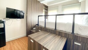 A compact hotel room with a bed, a TV mounted on the wall, and a desk. - Luxury And Minimalist Studio At Patraland Urbano Apartment (Bekasi)