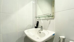 A bathroom with a white sink, a glass shelf above it, and a toilet to the right. - Luxury And Minimalist Studio At Patraland Urbano Apartment (Bekasi)