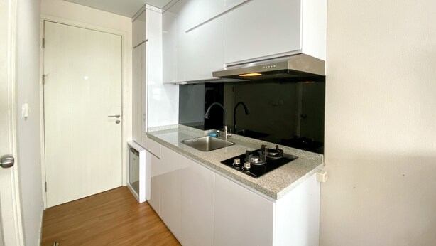 A compact kitchen with white cabinets, a stainless steel sink, and a black stove. - Luxury And Minimalist Studio At Patraland Urbano Apartment (Bekasi)